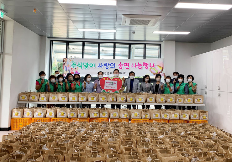 추석맞이 사랑의 송편 나눔행사 라고 적힌 현수막이 뒤에 걸려 있고 앞으로는 나눔행사할 물품들을 놓고 군수님과 부녀회회원들이 기념촬영을 하고 있다.