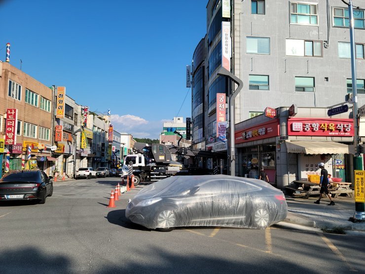 한 가게 앞에 보호비닐이 씌워친 한 차량이 주차되어 있다.