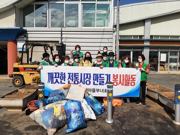 깨끗한 전통시장 만들기 봉사활동 이라고 적힌 현수막을 들고 기념촬영을 하고 있다