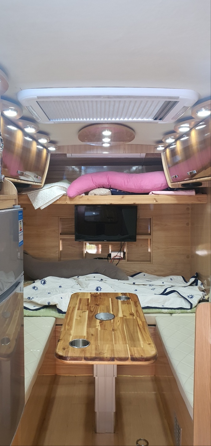 차량 내부의 모습을 찍은 사진이다. 캠핑 하면서 쉴 수 있는 내부 공간의 모습이다. 왼쪽에 냉장고가 있고 정면에는 tv가 그 위에 침실이 하나 있다.